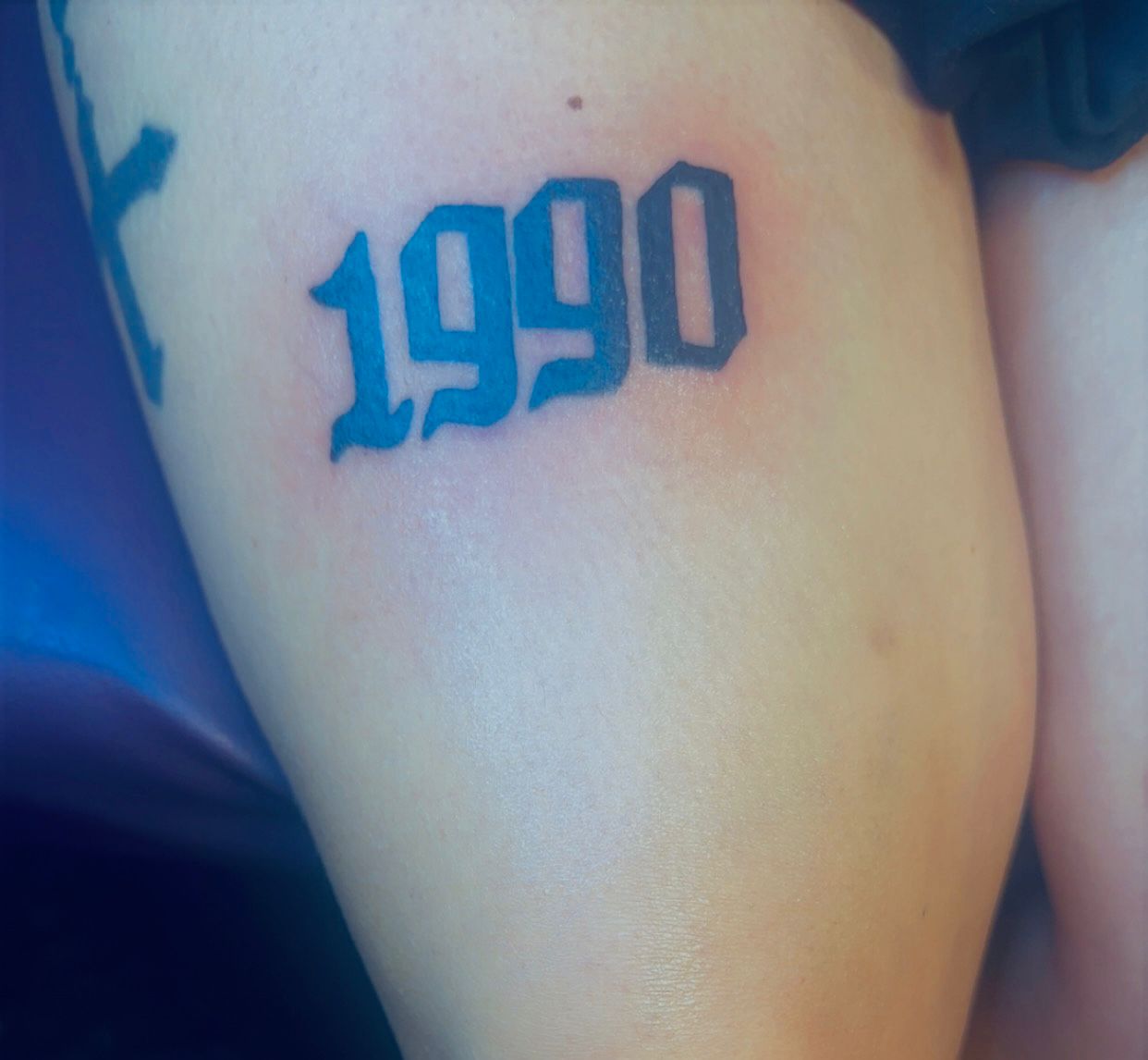 Tatouage lettering 1990 en typographie gothique old english sur cuisse Hakuna Tattoo Arpajon
