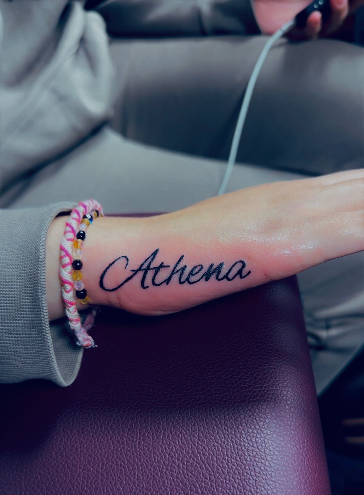 Tatouage lettering Athena en script cursif sur le cote de la main Hakuna Tattoo