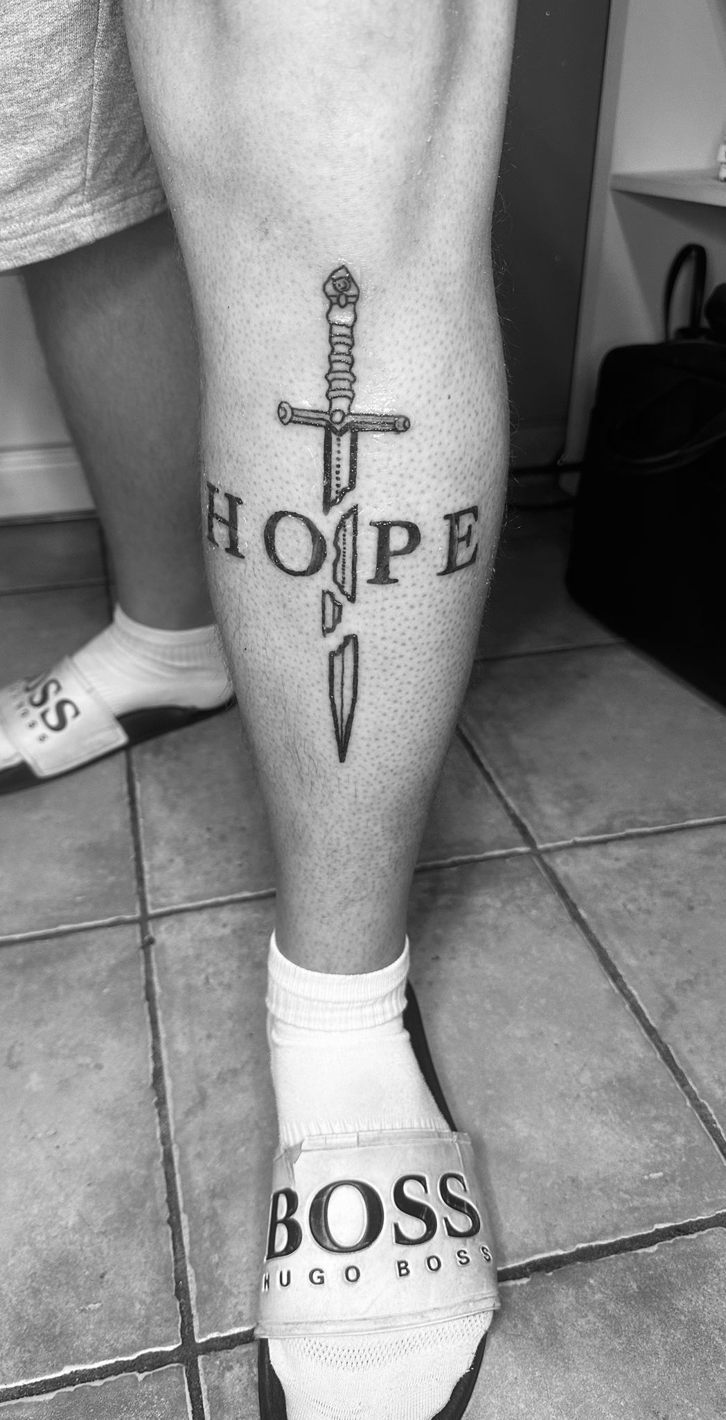 Tatouage lettering Hope avec epee gothique sur mollet Hakuna Tattoo Arpajon
