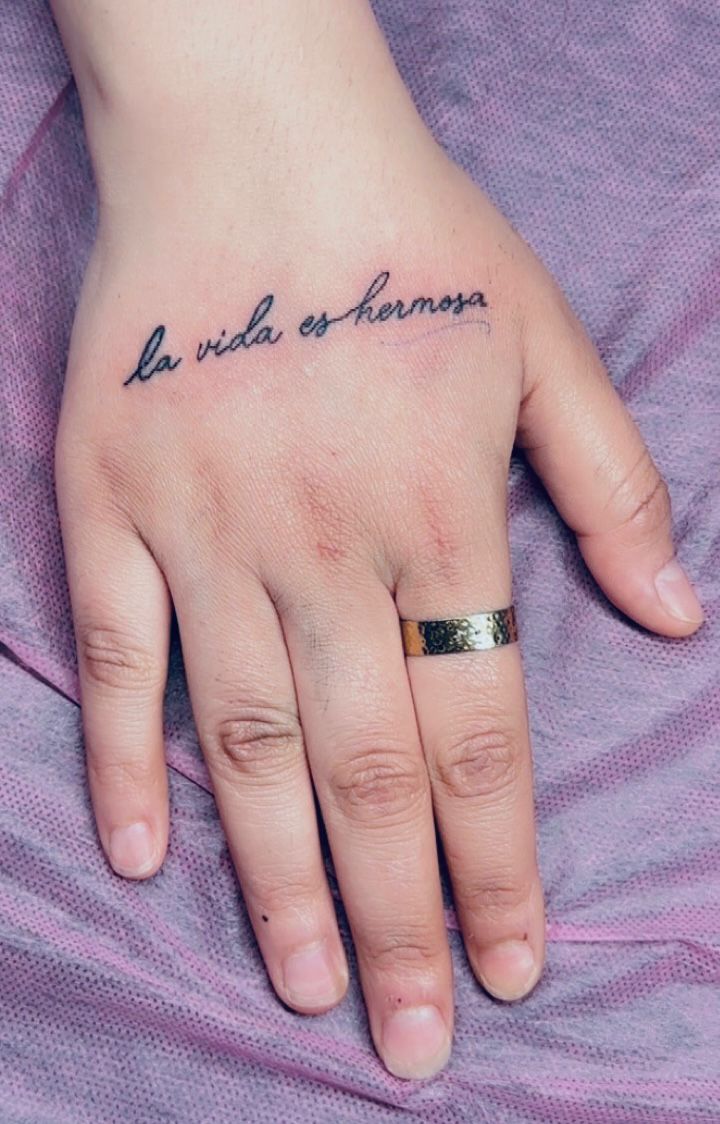Tatouage lettering la vida es hermosa en cursive fine sur dos de la main Hakuna Tattoo Arpajon