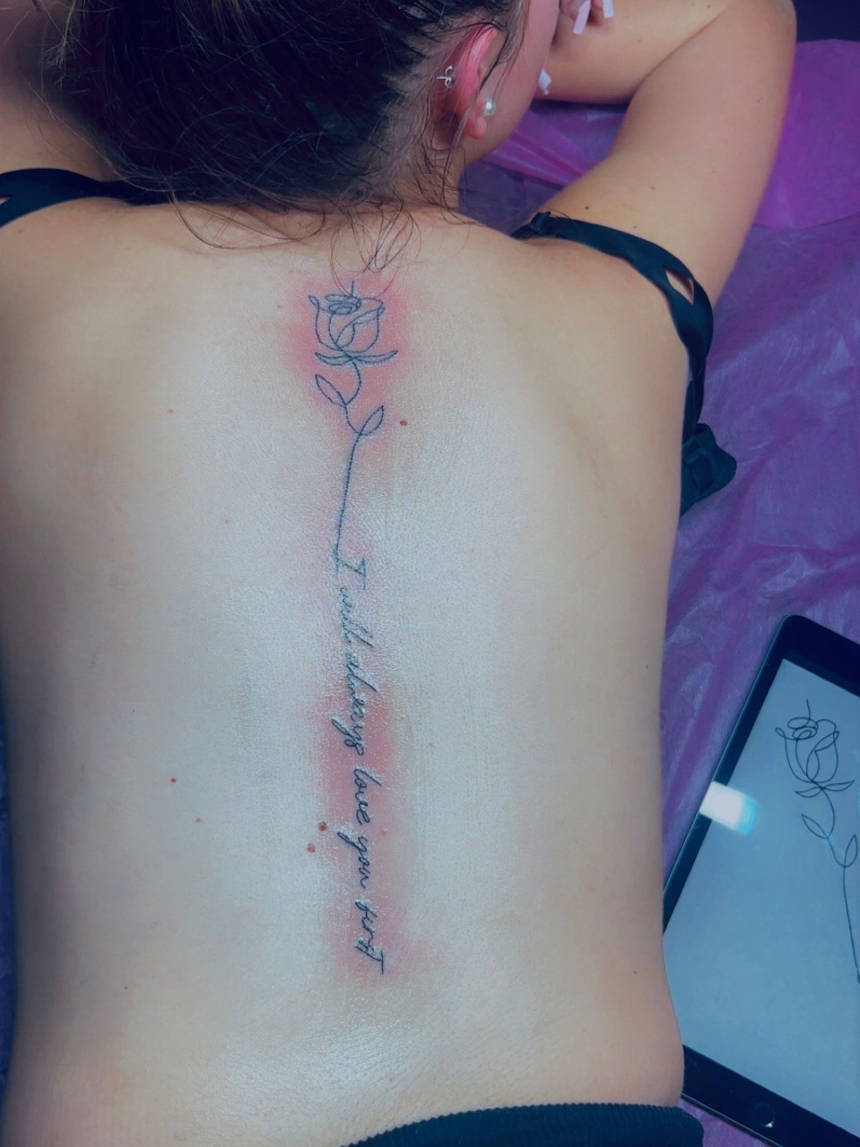Tatouage fineline rose le long de la colonne vertebrale avec citation en rouge et noir Arpajon